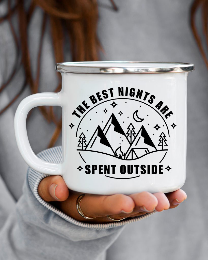 white coffee mug with a vinyl decal on the front reading "the best nights are spent outside" with a photo of mountains, stars, the moon and camping gear